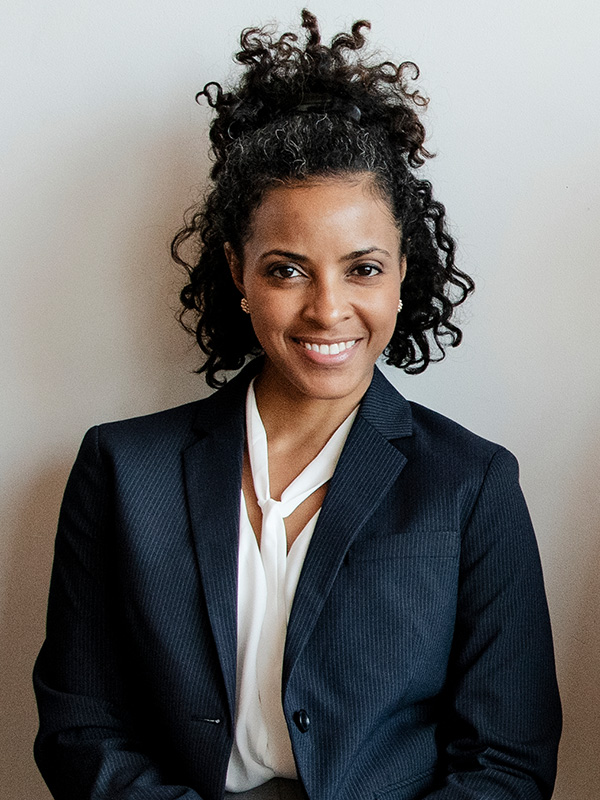 A woman with curly hair wearing a suit and smiling.